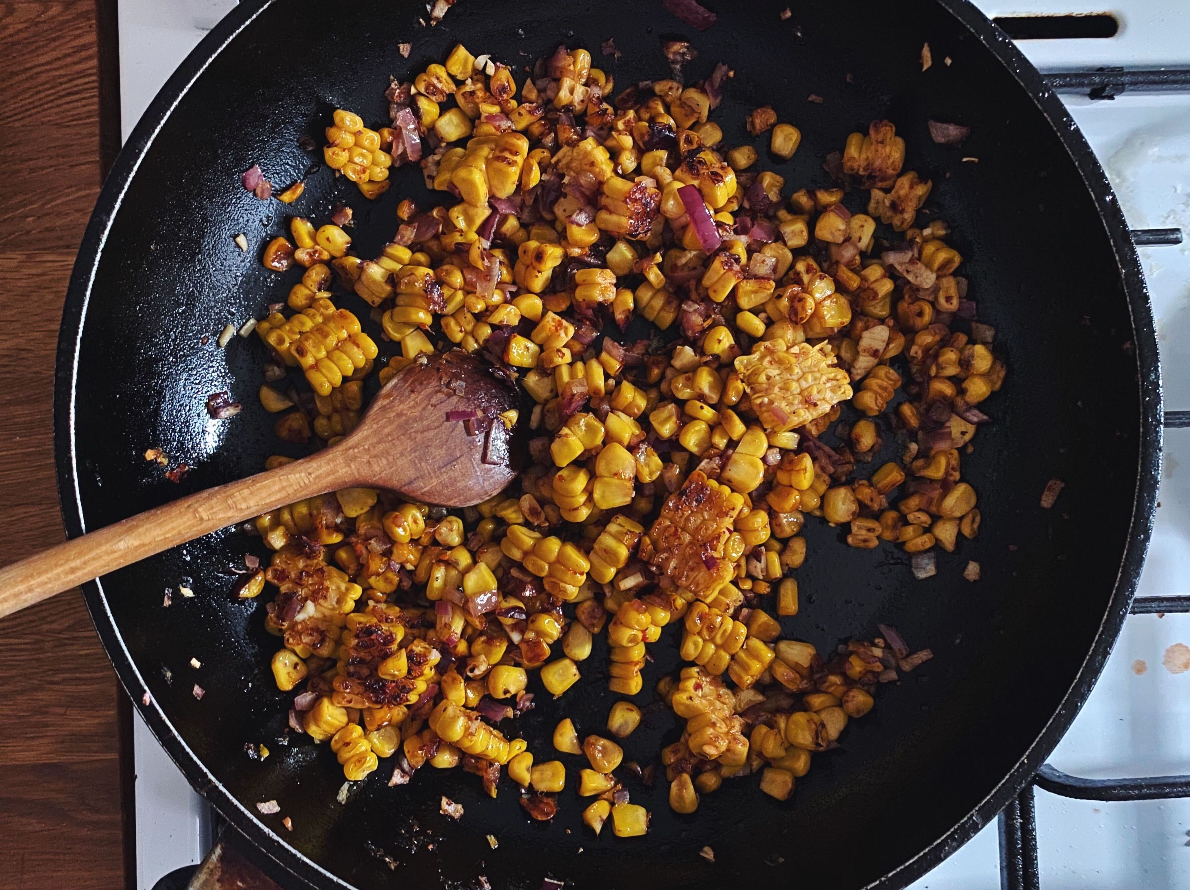 Während die Nudeln kochen Kirschtomaten halbieren. Zwiebel und Knoblauch schälen und fein hacken. Maiskörner vom Kolben schneiden – es ist kein Problem, wenn dabei kleinere und größere Stücke entstehen. Etwas Olivenöl in einer Pfanne bei mittlerer Hitze erwärmen. Mais ca. 5 Min. anbraten, bis er gebräunt und leicht knusprig ist. Chiliflocken, Zwiebel und Knoblauch dazugeben und weitere ca. 2 Min. anbraten, bis die Zwiebel glasig ist.