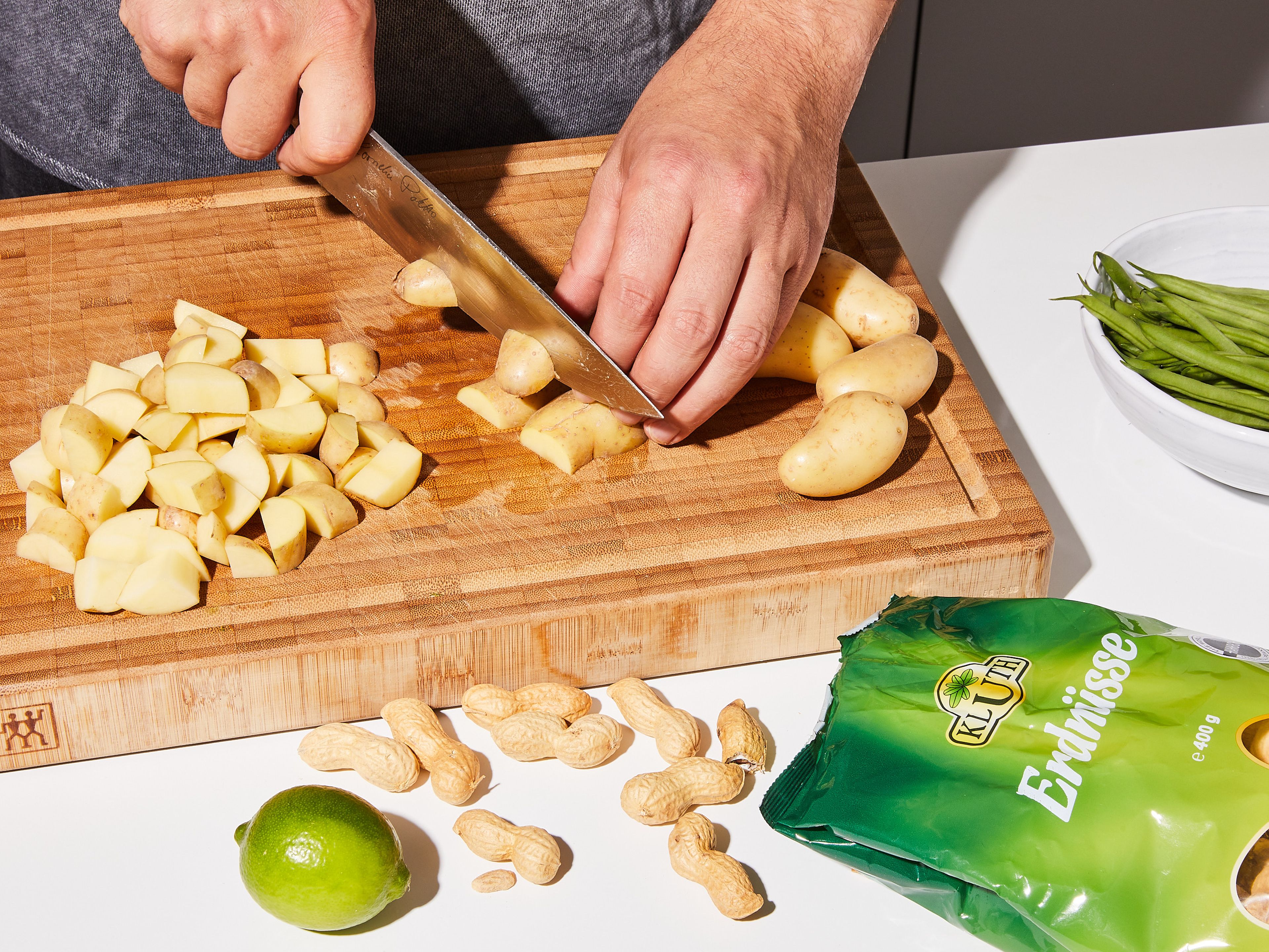 Peel the onion and cut into strips. Peel and finely chop garlic and ginger. Peel potatoes and cut into bite-sized cubes. Wash green beans, remove ends, and cut in half.