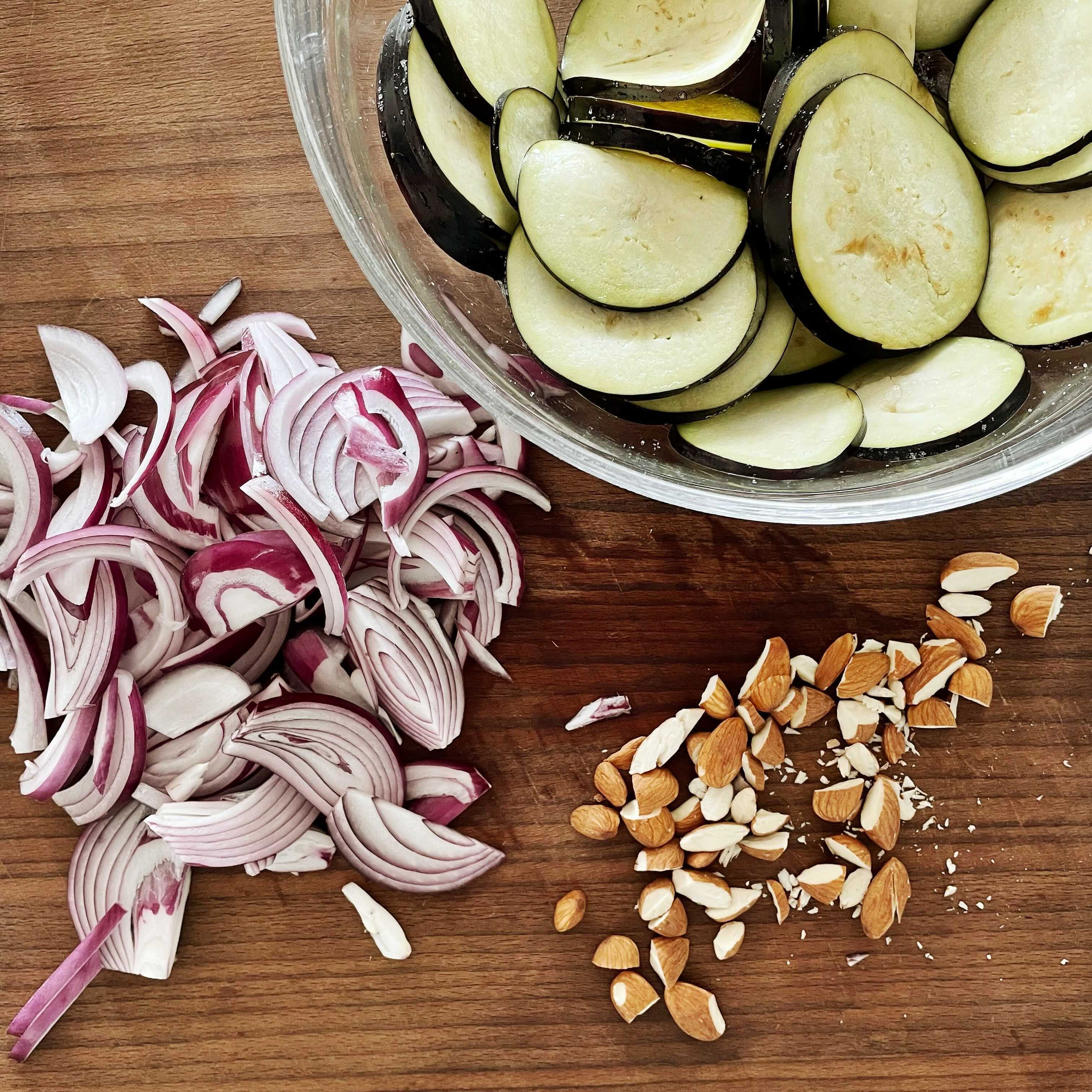 Wash the eggplant and cut into thin slices. Mix in a bowl with 1 tsp salt and let sit. Peel the onion and cut into fine slices. Remove the pomegranate seeds from the skin and roughly chop the almonds.