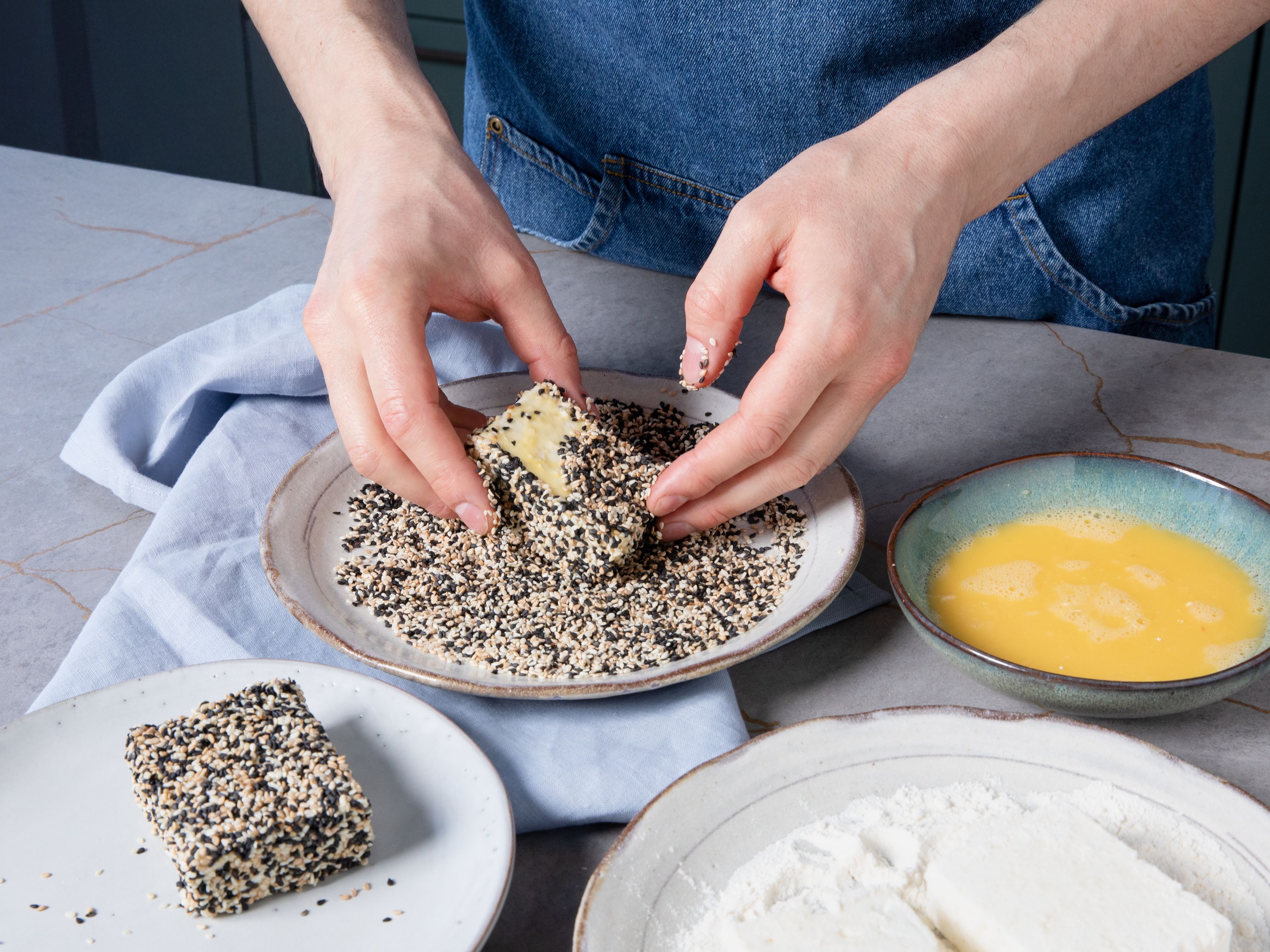 Halve each block of feta. Place flour on a plate. Beat egg in a small bowl. Combine white and black sesame seeds on a separate plate. Dredge feta pieces in flour, dip into the egg mixture, then coat thoroughly in the sesame mixture.