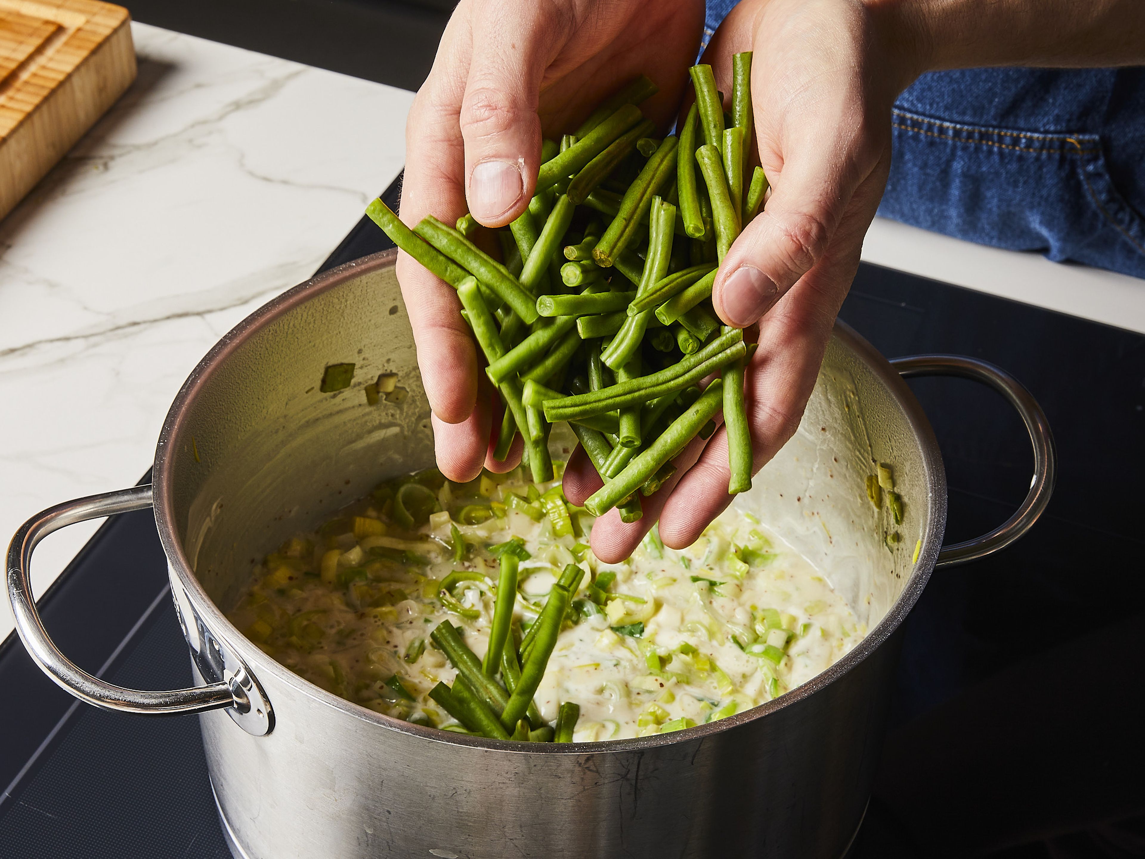 Add the vegetable stock and grainy mustard. Bring everything to a boil while stirring and then simmer uncovered for approx. 6–8 min. until the sauce is thick and the green beans are soft. Stir in the defrosted spinach, crème fraîche and finely chopped chives and parsley leaves. Then, remove the pot from the heat and season to taste with salt and pepper. If the mixture is too thick, add a little more water.