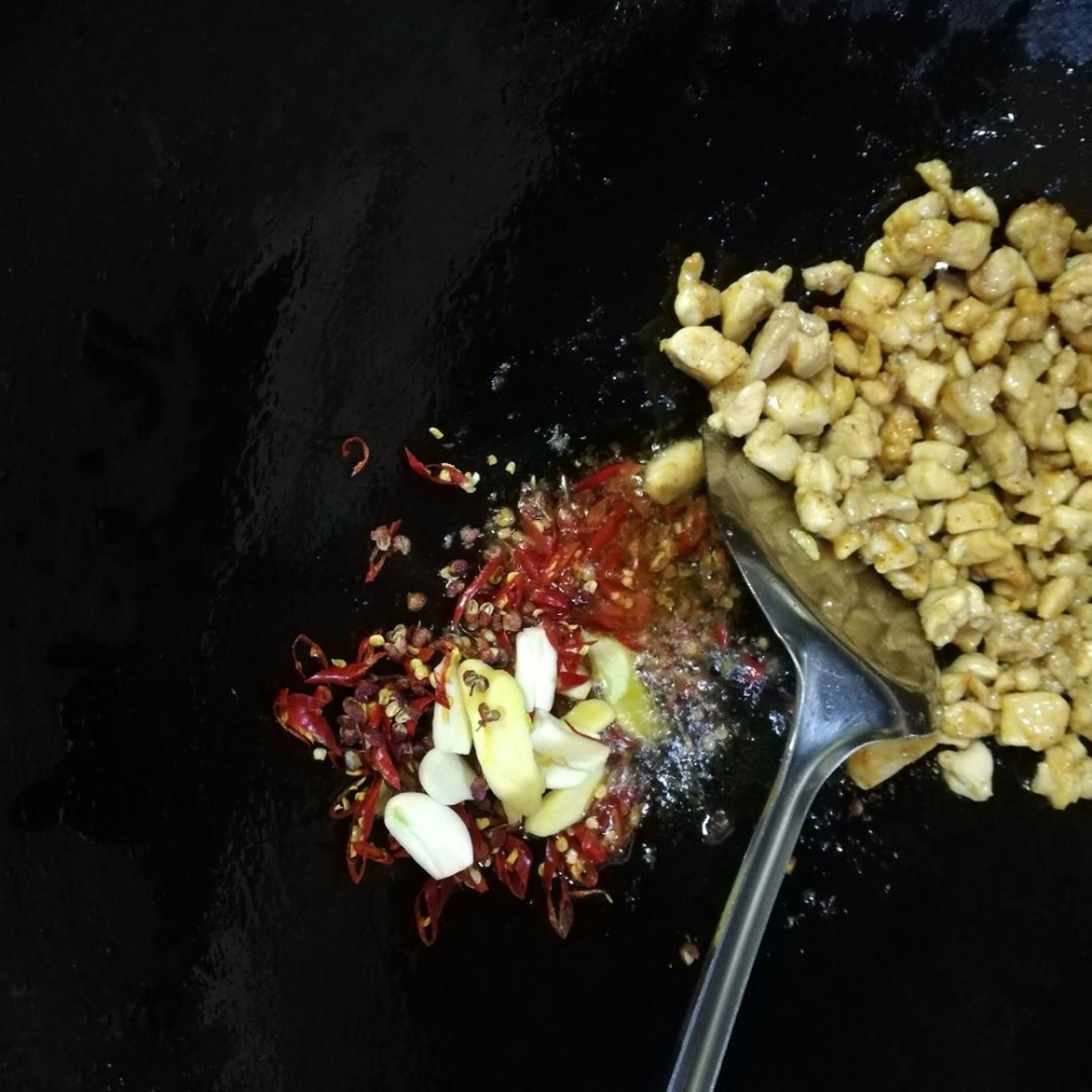 Add garlic, ginger, dried chilis, and Sichuan peppercorns to the wok, and fry.