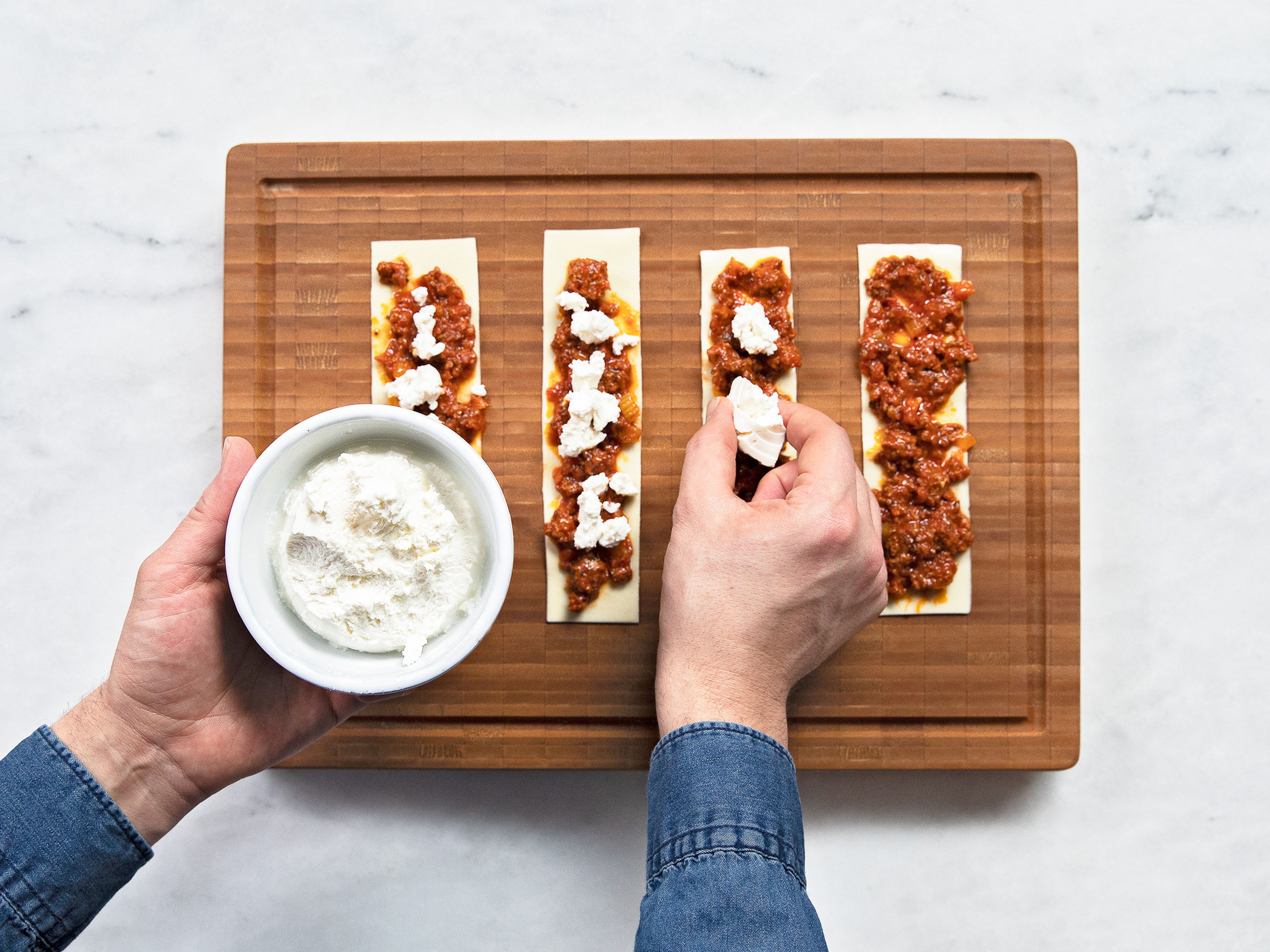 Preheat the oven to 180°C/355°F. Spread some cooled bolognese sauce over each lasagna sheet, discarding the bay leaves as you come across them. Spread ricotta cheese over and carefully roll the noodle up. Transfer rolls upright to a baking dish. Repeat until all the noodles are used up.