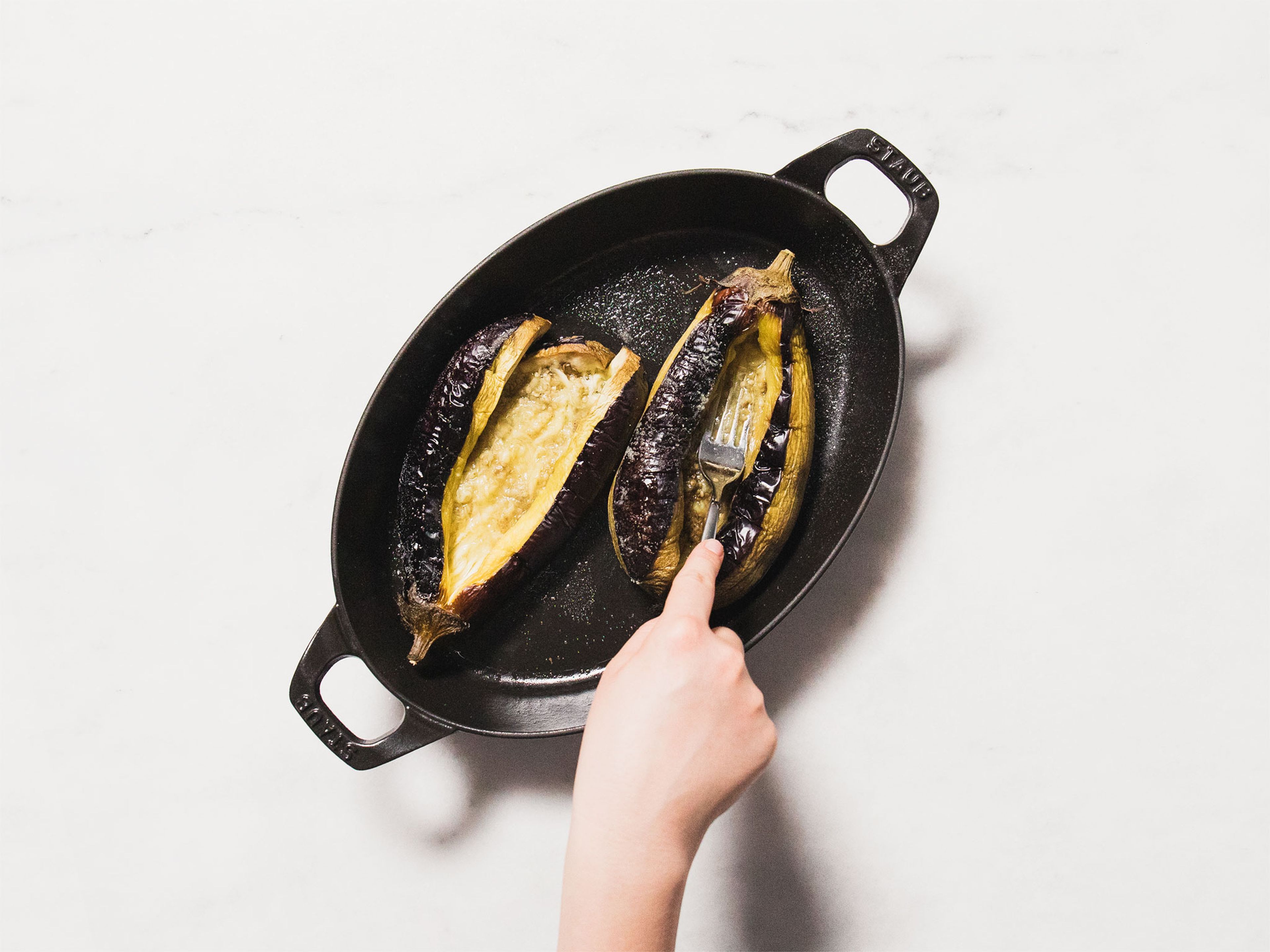Auberginen aus dem Backofen nehmen. Das Fruchtfleisch an der Stelle, die vor dem Backen leicht eingeschnitten würde, mit einer Gabel eindrücken, um Platz für die Füllung zu machen. Mit der Hackfleischmischung füllen.
